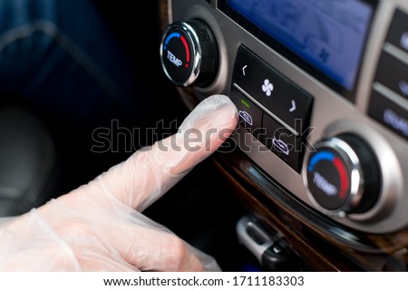 a hand in a medical glove presses the air recirculation button in the car, closing itself from outside air from the street Royalty-Free Stock Photo #1711183303