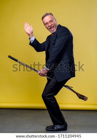 Senior man in suit sitting on a boom. Manager man playing funny games with a mop in studio.