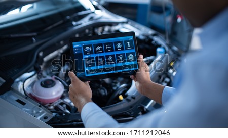 Car Service Manager or Mechanic Uses a Tablet Computer with a Futuristic Interactive Diagnostics Software. Specialist Inspecting the Vehicle in Order to Find Broken Components In the Engine Bay. Royalty-Free Stock Photo #1711212046