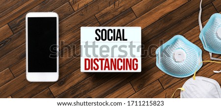 lightbox with message SOCIAL DISTANCING with smartphone and face masks on wooden background