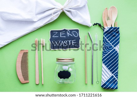 Zero waste concept. Cotton bags, bamboo cutlery, glass jars, metal straws and bathroom accessories on green background. Sustainable living. Eco friendly plastic free items. Top view.