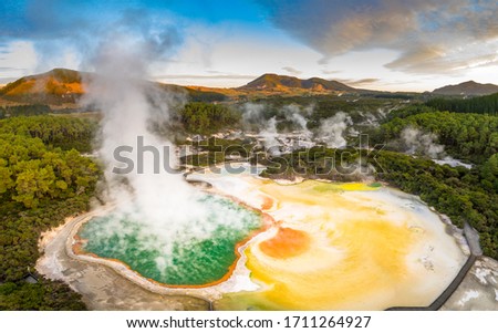 Aerial footage of hot sulphur springs at sunrise, showing colour splashed geothermal reserve of boiling water and steam evaporating in North Island of New Zealand Royalty-Free Stock Photo #1711264927