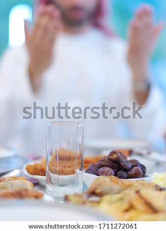 young arabian muslim man making traditional prayer to God, keeps hands in praying gesture before iftar dinner with family representing modern islam fashion and ramadan kareem concept