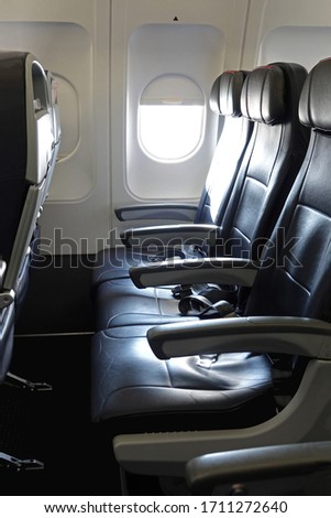 An empty row of three leather seats in the economy class section of a commercial airliner jet is shown in a vertical view during the day.
