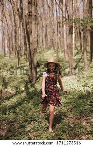 Little girl in a straw hat and in a sundress walks through the spring forest. Children's vacation in nature. The child plays in the forest.