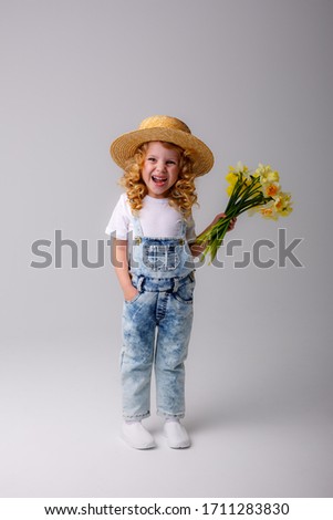 a small curly haired girl in a straw hat holds a bouquet of spring flowers on a white background