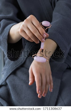 Jade roller massage tool in a female hands . Pink gua sha facial massager. Vertical photo with copy space.