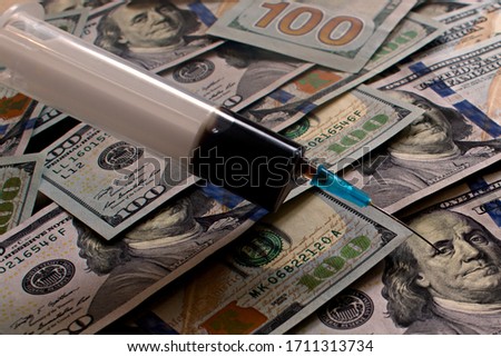 syringe with the liquid oil like pierces a hundred dollar bill