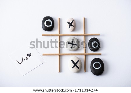 top view of tic tac toe game with grid made of paper tubes, pebbles marked with crosses and naughts, and card with win inscription on white surface