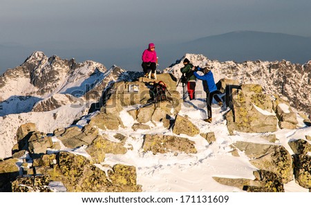 Couple of climbers is taking pictures on the summit of Rysy mountain in winter, High Tatras, Slovakia