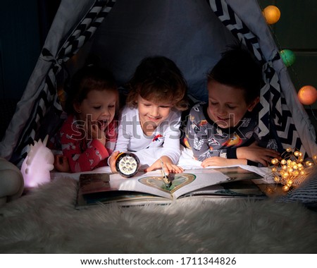 Three children sit in a tent at night and read by the light of a flashlight an interesting book about the adventures of "treasure Island". The pirate game. Learning to read in a playful way.