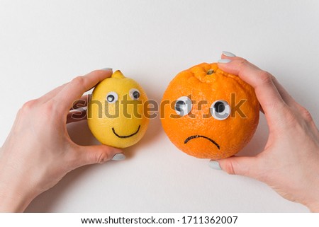Hands holding lemon and orange with character. Food with funny face on white background.