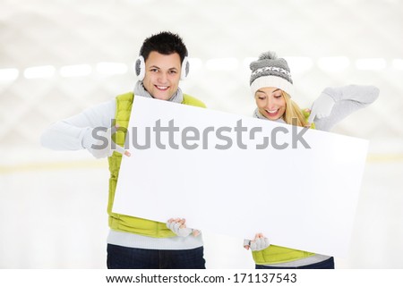 A picture of a young couple showing a white board in the ice rink