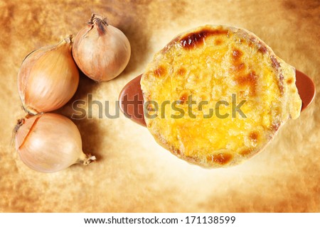 A picture of a bowl of onion soup presented over rustical background