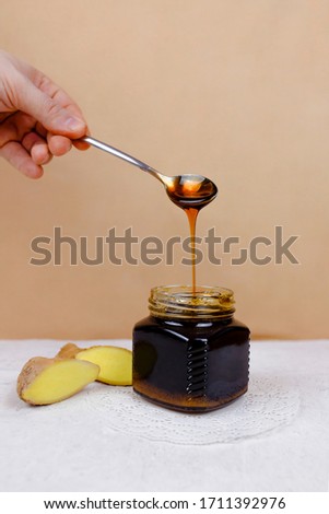 Buckwheat honey pours from spoon into jar and sliced ginger lying near. Natural medicine, healthy food, ethnoscience, strengthening immunity. Vertical picture, close-up, selective focus.