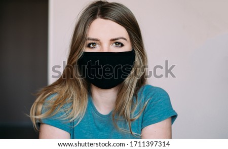
young woman in a black medical mask in a turquoise t-shirt with blond hair and dark eyes on a light background. quarantine. Coronovirus covid-19 concept pandemic epidemic. Stay at home Royalty-Free Stock Photo #1711397314