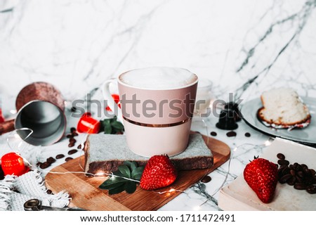 yummy coffee presentation at home in isolation. full Cup of milk froth on a marble table with a Turkish coffee pot, scattered coffee beans, coffee capsules, strawberries, candles and garlands
