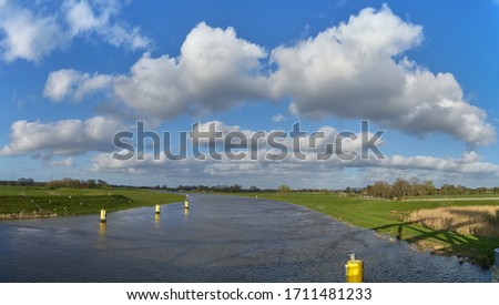 panorama view from the bridge over the river Hunte in the village Huntebrück (district Wesermarsch, Germany) on a bright sunny spring day with vivid blue sky and beautiful white clouds
