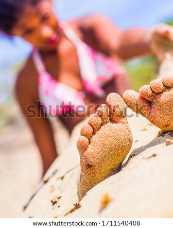 feet out of the sand, little girl with pink costume on the beach plays with the sand