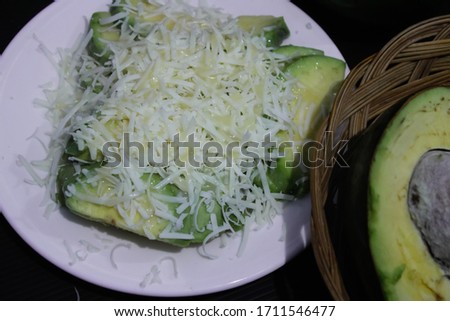Avocado salad. Avocado cut, rated cheese and milk on white plate. and beside the plate there is basket and avocado fruit