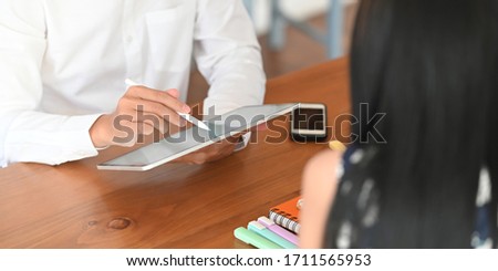 Photo of young couple relaxing and working with computer tablet while sitting together at the wooden working desk over comfortable living room as background.