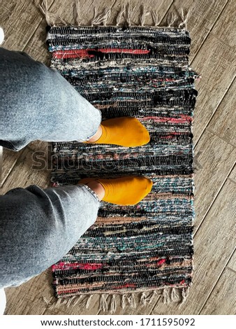 Man stands on the carpet and takes pictures of his feet.
Background and texture. Photo of legs in yellow socks and jeans, top view. 
Restored old handmade rug with colored stripes for background. 
