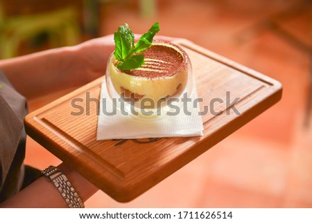 Waiter holding tray with tasty dessert. Traditional Italian dessert Tiramisu. Waitress in uniform at work. Restaurant or cafe service.