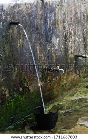 Water station in a country site showing water supply system in a mountainous area. Washing place of local people in a village. Vertical photo shows green lichen developed by moisture