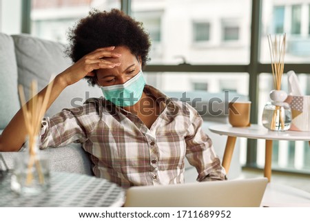 Worried African American woman wearing face mask while working on a computer at home. 