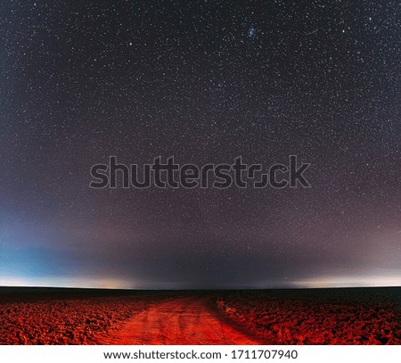 Night Starry Sky With Glowing Stars Above Country Road Is Lit In Red. Countryside Field Landscape.