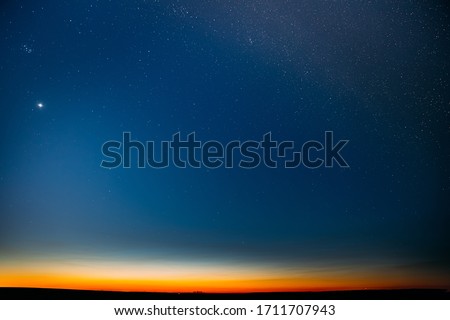 Night Starry Sky With Glowing Stars Above Countryside Field Landscape In Early Spring. Bright Glow Of Planet Venus In Sky Among The Stars. Sky In Warm Lights Of Evening Sunset Dawn Or Morning Sunrise.