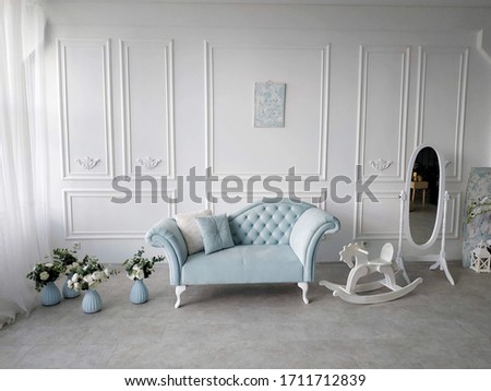The interior is in the Baroque style. Vintage sofa with carriage tie, upholstered in blue pastel velvet with decorative pillows. The room has blue vases with roses and eucalyptus, a wooden rocking hor
