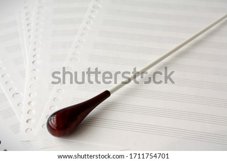 Conductor's baton with white shaft and two-toned wooden grip handle on sheets of blank music manuscript papers Royalty-Free Stock Photo #1711754701