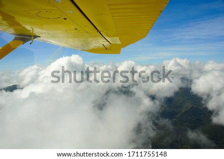 Aerial view from a bright yellow,  aircraft. Beautiful scene with wing tip,  blue sky and soft fluffy clouds