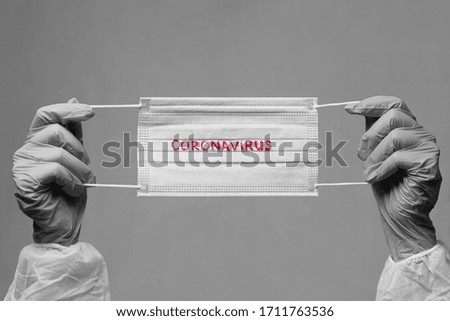 Medical surgical protective face mask with a red inscription CORONAVIRUS in hands wearing gloves.  black and white image. Covid -19 pandemic concept. Copy space.