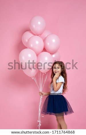 surprised adorable little child girl posing with pastel pink air balloons isolated over pink background. Beautiful happy kid on a birthday party.