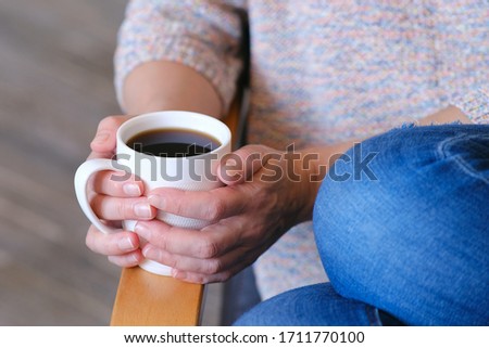 Hot coffee in a Cup. The girl holds a Cup of coffee in her hands. Warms your hands. Sitting in a chair at home in quarantine