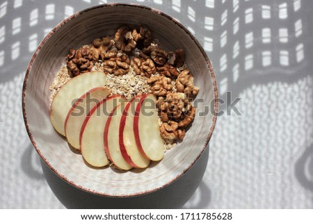 Apple Walnut Oatmeal in vintage bowl on white wooden table background. Natural lighting. Beautiful openwork shadow from the curtain. Top view.