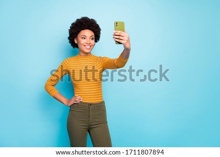 Photo of beautiful wavy lady hold telephone hands making selfies for new post good mood wear yellow striped shirt pants isolated blue color background