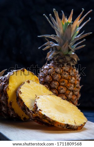 Pineapple cut in a board with a black background, fruit cut in slices together with a whole pineapple. Vertical. Healthy food concept.