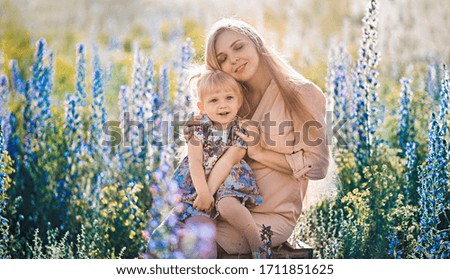 Beautiful blond woman with long hair with her little daughter in a flowering field
