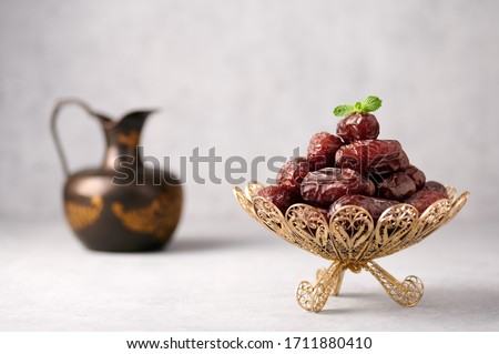 Date Fruits or Kurma in vintage arabic dish and jug of water at grey concrete background. Dates and water is Ramadan meal. Ramazan Iftar food. Royalty-Free Stock Photo #1711880410