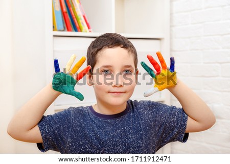 A child with painted colored fingers shows his hands sitting 