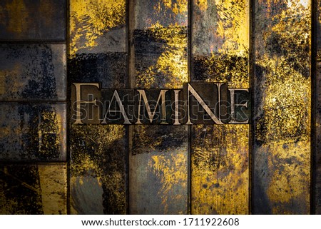 Photo of real authentic typeset letters forming Famine text on vintage textured grunge copper and gold background
