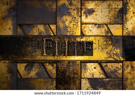 Photo of real authentic typeset letters forming Elite text on vintage textured grunge copper and gold background