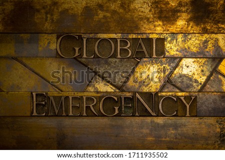Photo of real authentic typeset letters forming Global Emergency text on vintage textured grunge copper and gold background