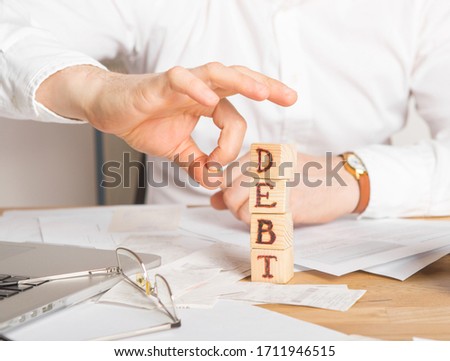 Businessman removes wooden blocks with the word Debt. Reduction or restructuring of tax. Bankruptcy announcement. Refusal to pay loans and invalidate them. Royalty-Free Stock Photo #1711946515