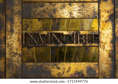 Photo of real authentic typeset letters forming Invincible text on vintage textured grunge copper and gold background