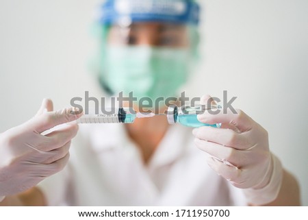 Close up medical doctor wearing face shield, medical mask and medical grove. She holding draw syringe and bottle with Coronavirus vaccine for 2019-nCoV COVID virus.