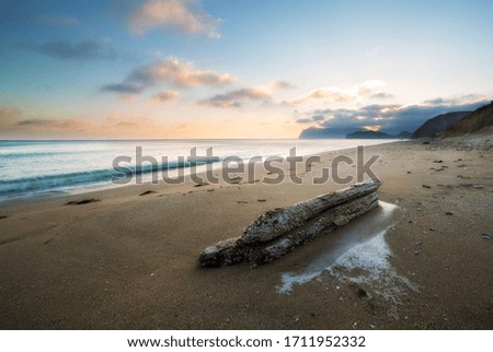 Landscape on a sandy beach with a log at sunset and mountains on the horizon